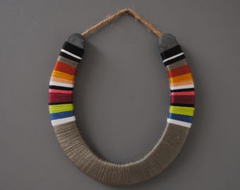 May include: A horseshoe wrapped in grey yarn with colourful stripes of red, orange, yellow, green, blue, pink, black and white yarn.