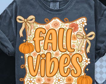 May include: Dark gray t-shirt with a colorful fall-themed graphic. The design features the words "FALL VIBES" in orange, surrounded by pumpkins, flowers, and bows. The shirt has a vintage, slightly faded look.