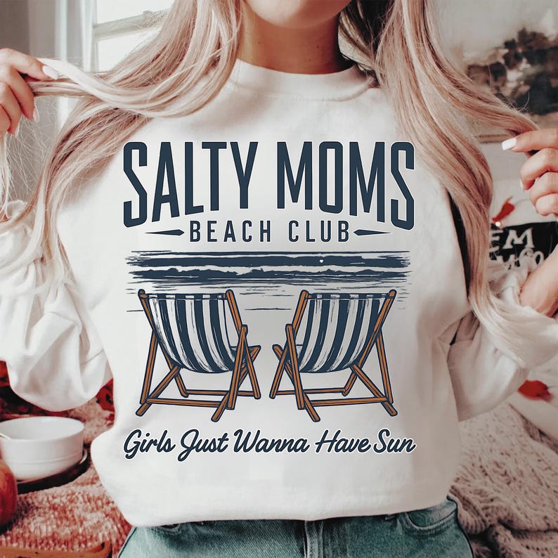 May include: White sweatshirt with a graphic design that says "Salty Moms Beach Club" with two beach chairs and the text "Girls Just Wanna Have Sun".