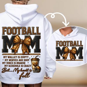 Könnte beinhalten: Weißer Hoodie mit dem Text "FOOTBALL MOM" in Braun und Schwarz. In der Mitte befindet sich eine braune Schleife mit goldenen Sternen. Darunter stehen die Worte "MY WALLET IS EMPTY" und "But... My heart is full". Eine Kaffeetasse und ein Footballhelm sind ebenfalls abgebildet.