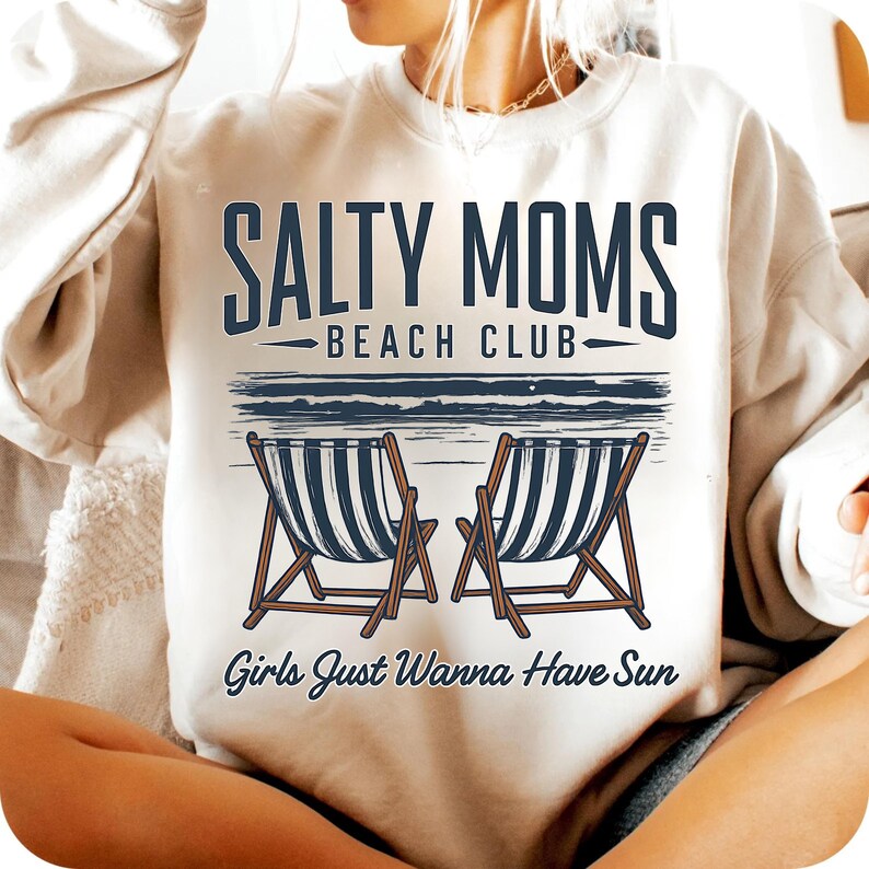 May include: White sweatshirt with the text "Salty Moms Beach Club" and "Girls Just Wanna Have Sun" in black lettering. The graphic also features two beach chairs with blue and white stripes.