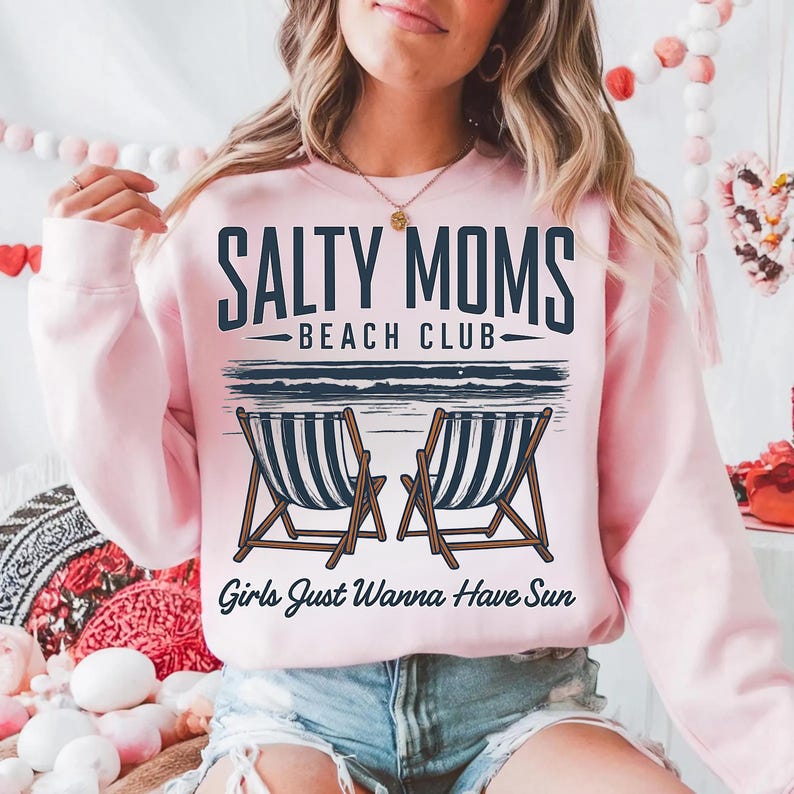 May include: Pink sweatshirt with the text "Salty Moms Beach Club" and "Girls Just Wanna Have Sun" in a vintage style graphic. The graphic also features two beach chairs.