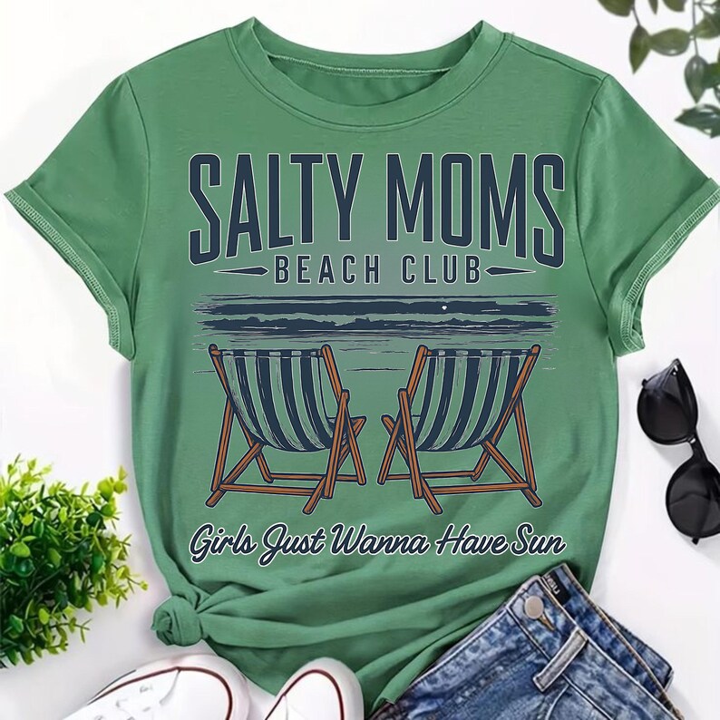 May include: Green short-sleeved t-shirt with the text "Salty Moms Beach Club" and an illustration of two beach chairs on a beach. The text "Girls Just Wanna Have Sun" is below the illustration.