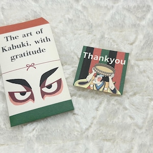 以下が含まれることがあります： 白いテクスチャのある表面に、2枚の日本のテーマのカードがあります。1枚のカードには「The art of Kabuki, with gratitude」の文字と様式化された目があります。もう1枚のカードには、歌舞伎役者のイラストとともに「Thankyou」と書かれています。