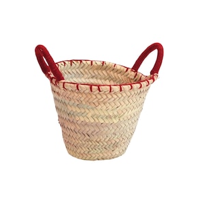 Peut inclure: Un petit panier tressé de couleur beige naturel. Il est doté de deux anses rouges et d'une bordure rouge sur le bord supérieur. Le panier est fait d'un matériau tissé, idéal pour transporter des objets.