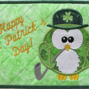 May include: Green quilted fabric with a green and white embroidered owl wearing a green hat with a shamrock. The owl is holding a pipe and the fabric says "Happy St. Patrick's Day!"