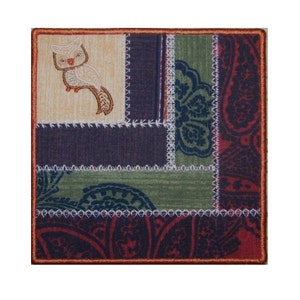 Può includere: Un blocco di patchwork quadrato con un gufo ricamato nell'angolo in alto a sinistra. Il blocco è realizzato con diversi tessuti in tonalità di marrone, verde, viola e rosso. I tessuti sono cuciti insieme con una cucitura bianca.