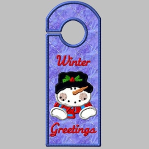 May include: A purple door hanger with a snowman design. The snowman is wearing a black hat with holly and a red scarf. The text "Winter Greetings" is embroidered in red.