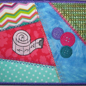 May include: A colorful patchwork fabric square with a pink measuring tape, three buttons, and a green and gold patterned fabric in the corner.