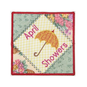 Può includere: Un cerotto ricamato quadrato con un ombrello giallo e rosso e il testo "April Showers" in rosa.