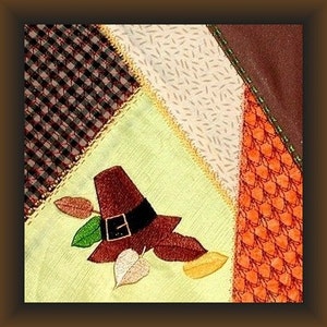 Può includere: Un cappello da pellegrino marrone con una fibbia nera è ricamato su uno sfondo di tessuto verde chiaro. Il tessuto fa parte di una trapunta patchwork più grande con tessuti marroni, beige e arancioni.
