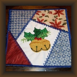 Peut inclure: Un carré de tissu blanc avec une bordure bleue, orné d'un motif brodé de deux cloches dorées avec un brin de houx vert. Le carré de tissu est assemblé avec d'autres tissus en rouge, bleu et crème.