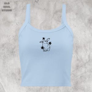 May include: A light blue tank top with a black outline of a rabbit surrounded by stars.