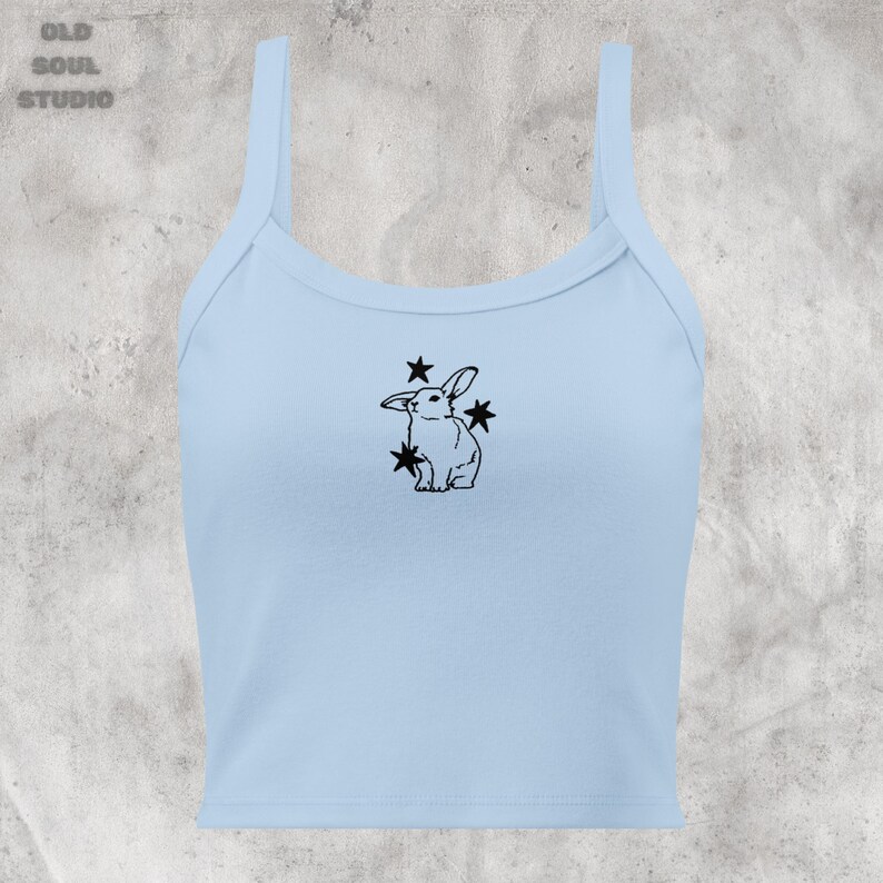 May include: A light blue tank top with a black outline of a rabbit surrounded by stars.