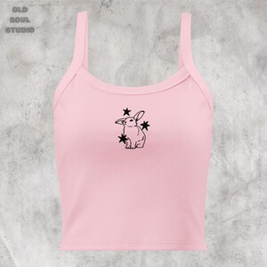 May include: A pink sleeveless crop top with a black outline of a rabbit with stars around it.