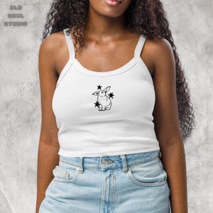 May include: A white crop top tank with a black outline of a rabbit with stars around it.