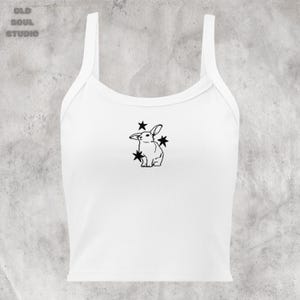May include: White crop top with a black line drawing of a rabbit surrounded by stars.