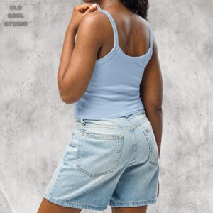 May include: A light blue tank top with thin straps and a cropped fit. The tank top is paired with light blue denim shorts.