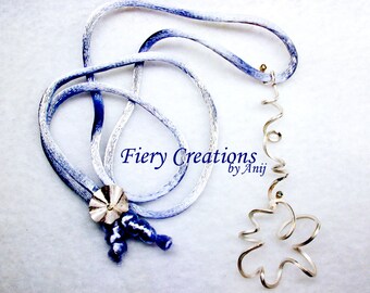 May include: A silver necklace with a blue and white ombre cord and a silver pendant shaped like a flower. The pendant is made of wire that is twisted and curled. The necklace is labeled "Fiery Creations by Anji".