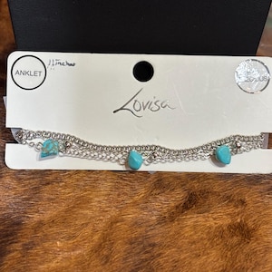 May include: Silver anklet with turquoise-colored stones. The anklet is 11 inches long and features three strands of chain. The brand name "Lovisa" is printed on the packaging.