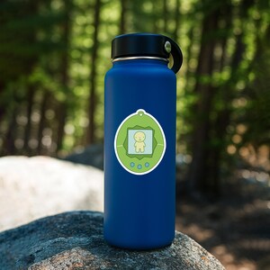 May include: A blue water bottle with a black lid and a green sticker. The sticker features a light green frame with a yellow figure inside. Below the frame are three small green circles. The bottle is sitting on a rock.