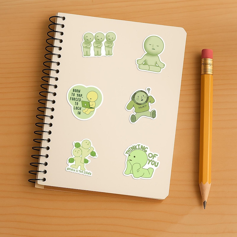 May include: A spiral-bound notebook with several green character stickers and a yellow pencil. The stickers feature various poses and phrases, including "Thinking of You" and "Born to Yap, Forced to Lock In."