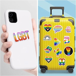 Może przedstawiać: Białe etui na telefon z naklejką LGBT i ż&oacute;łta walizka pokryta kolorowymi naklejkami Pride. Naklejki zawierają tęcze, serca i słowo "Pride".
