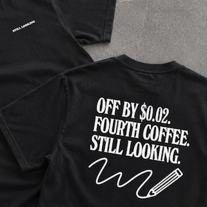 May include: A black short-sleeved t-shirt featuring white text on the front chest that reads STILL LOOKING. The back of the shirt displays the white text OFF BY $0.02. FOURTH COFFEE. STILL LOOKING. accompanied by a white graphic of a pencil.