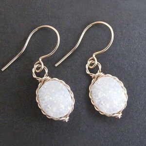 May include: A pair of gold wire wrapped earrings with white oval-shaped stones.