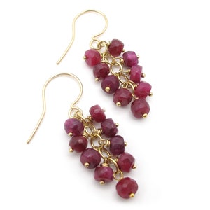 May include: A pair of gold dangle earrings with a cluster of ruby red gemstone beads.