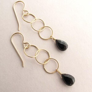 May include: Gold earrings with black teardrop gemstones and a chain of linked circles.