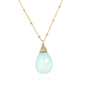 May include: A delicate gold chain necklace with a light blue teardrop-shaped gemstone pendant.
