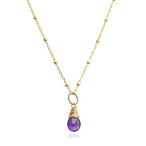 May include: A delicate gold chain necklace with a small purple amethyst gemstone pendant. The pendant is wrapped in gold wire.