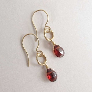 May include: A pair of gold earrings with red gemstone drops. The earrings have a simple wire design and are perfect for everyday wear.