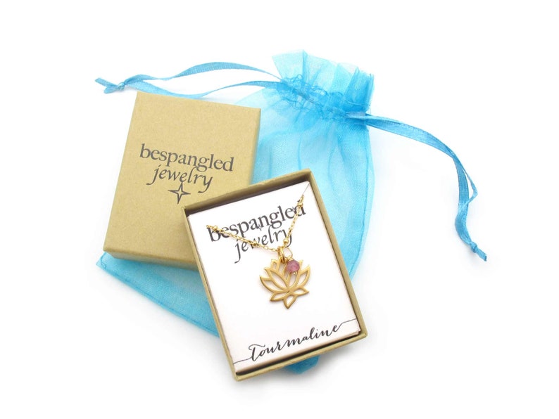 Bespangled Jewelry openwork gold lotus flower pendant necklace with pink tourmaline charm accent packaged in a small kraft jewelry gift box with teal organza pouch. Ready for gift-giving!

Necklace card says tourmaline with Bespangled logo.