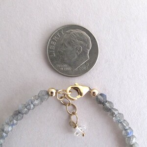 Pu&ograve; includere: Un delicato braccialetto di perline con piccole pietre preziose grigio-blu sfaccettate. Il braccialetto ha una chiusura color oro e un piccolo ciondolo di cristallo trasparente. Una moneta &egrave; inclusa per riferimento.