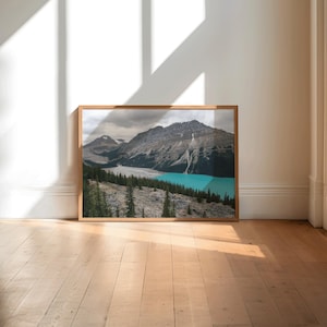 Peut inclure: Photographie encadrée d'un paysage de montagne, d'un lac turquoise et de conifères. La photo est dans un cadre en bois et est exposée sur un sol en bois clair. L'image est bien éclairée par la lumière naturelle.