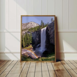 May include: A photograph of a waterfall cascading down a rocky cliff face in a lush green forest. A rainbow arches over the water at the base of the waterfall.