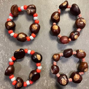 May include: Four circular bracelets made from dark brown horse chestnuts and colorful beads. Two bracelets feature alternating bright orange and light gray spherical beads, while the other two feature striped orange and white cylindrical beads.