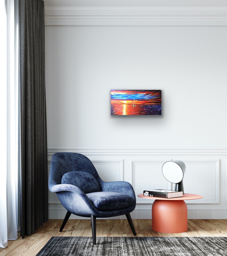 May include: A painting depicting a sunset over the ocean, with a sailboat visible in the distance. The sky is a blend of orange, red, and purple hues, while the water is a deep blue. The painting is framed and hangs on a white wall.