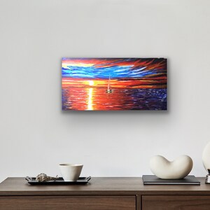 May include: A painting depicting a sailboat on the water at sunset. The sky is a blend of orange, red, and blue with clouds. The water is a dark blue with reflections of the sunset.