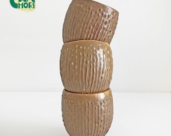 May include: Three stacked, textured, brown ceramic pots. Each pot has vertical grooves and small, evenly spaced bumps. The pots are a warm, earthy tone, and the logo "CHA MORE" is visible in the upper left corner.