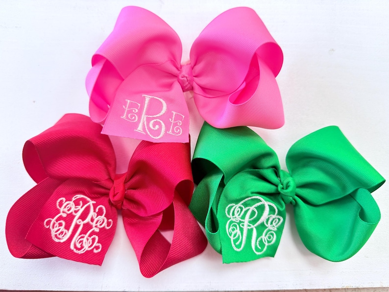 Bright color hair bows, made of grosgrain ribbon. Monogram initials shown in white thread. Hair bows are pink, red, and green.