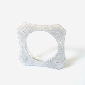 Può includere: Un anello d'argento di forma quadrata con quattro piccoli diamanti incastonati nella fascia.