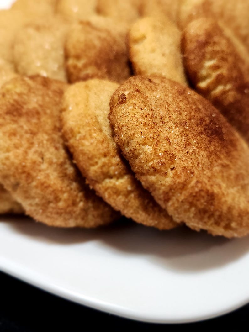 May include: A close-up of a plate of freshly baked cinnamon sugar cookies. The cookies are golden brown and have a slightly crispy texture.