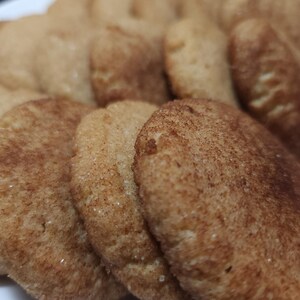May include: A close-up of a pile of freshly baked cinnamon sugar cookies. The cookies are golden brown and have a slightly crispy texture.