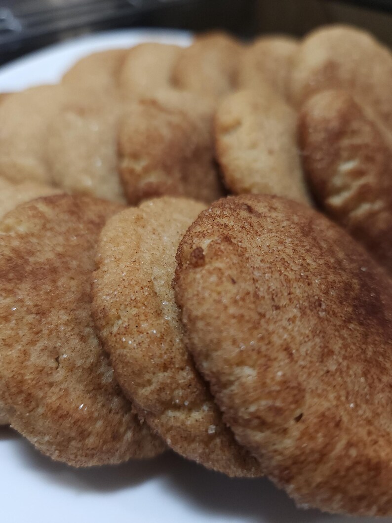 May include: A close-up of a pile of freshly baked cinnamon sugar cookies. The cookies are golden brown and have a slightly crispy texture.