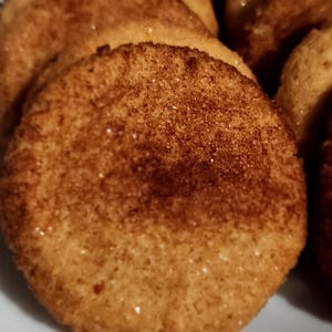 May include: Close-up of a pile of golden brown cookies with a cinnamon sugar topping.