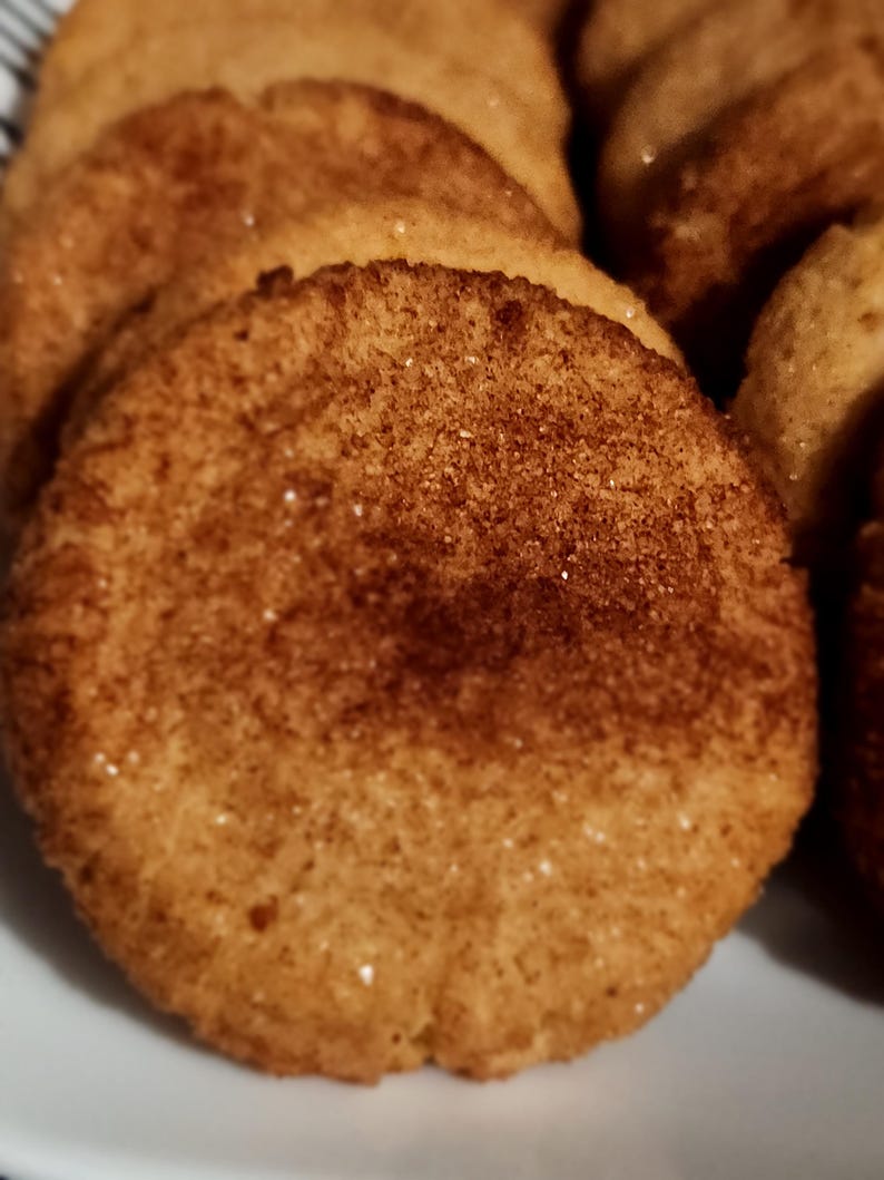 May include: Close-up of a pile of golden brown cookies with a cinnamon sugar topping.