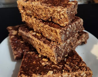 May include: A stack of chocolate rice crispy treats on a white plate. The treats are rectangular, with a dark chocolate coating and visible rice cereal and nuts. The treats are stacked on top of each other.